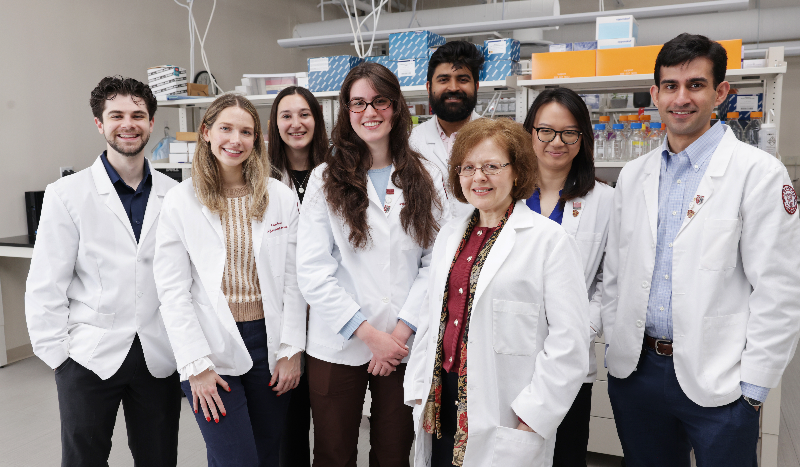 students in white lab coats standing with professor in lab